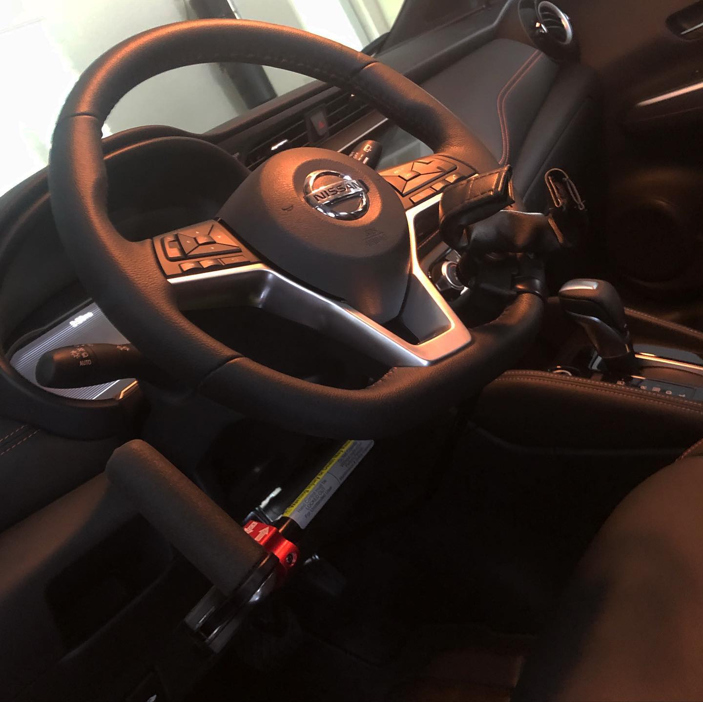 The interior of the Nissan Kicks showing the newly installed hand-control mechanism, a black lever and linkage mounted on the steering column beside the wheel and connecting down toward the pedals.