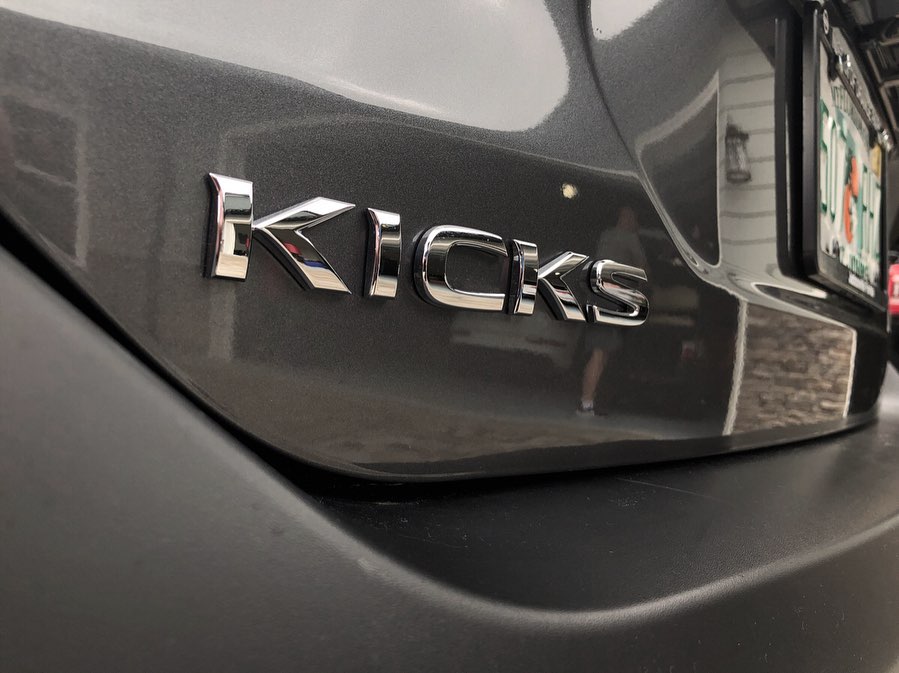 A close-up of the chrome Kicks lettering on the rear hatch of the gray Nissan.