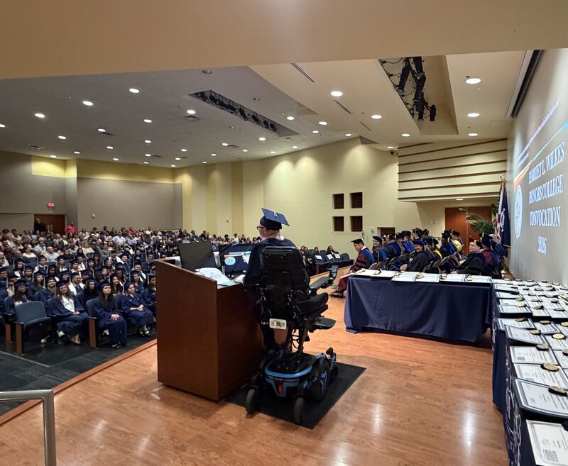 Ryleigh Newman speaking from a podium in his power wheelchair at Convocation.