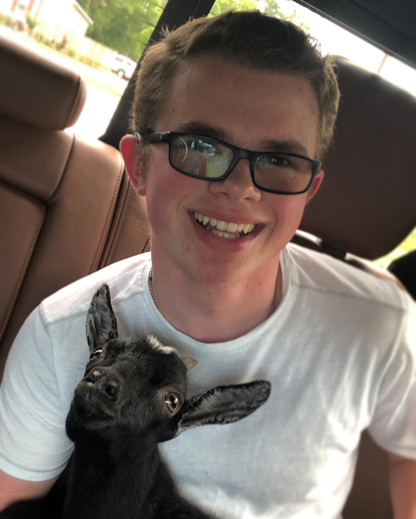 Ryleigh Newman grinning in a car back seat with a small black goat kid tucked against his chest.