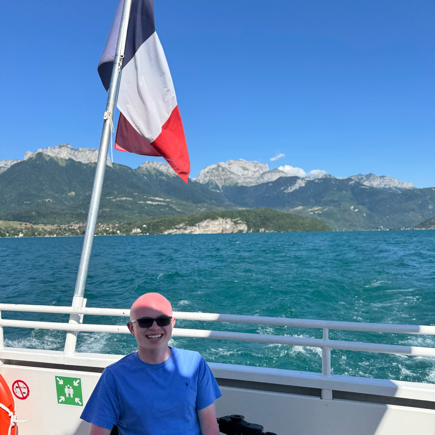 A turreted lakeside chateau on a wooded point of Lake Annecy, with bare alpine peaks rising behind the deep blue water.